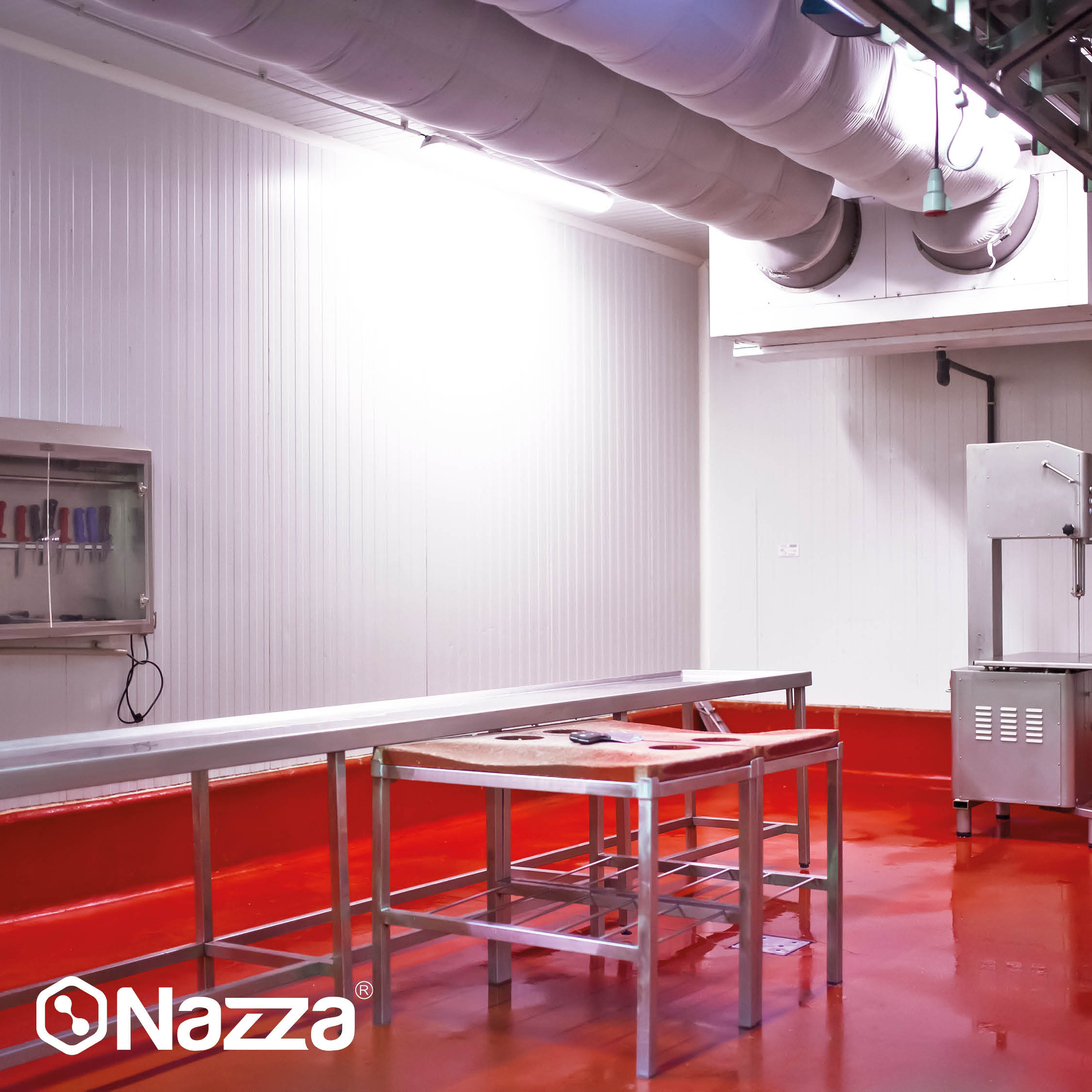 La imagen muestra una sala de despiece o área de trabajo alimentario con paredes blancas y suelo rojo brillante, recubierto con pintura epoxi alimentaria para facilitar la limpieza e higiene. Hay mesas de acero inoxidable, una máquina de corte industrial y, en la pared, un gabinete con cuchillos organizados, además de conductos de ventilación en el techo.