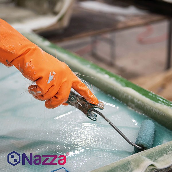 persona aplicando resina sobre una pieza de fibra de vidrio. La persona lleva un guante naranja de protección y está usando un rodillo para extender la resina de manera uniforme sobre la superficie. La pieza parece estar en proceso de laminado, con la fibra de vidrio visible en la base, lista para ser impregnada con la resina. El entorno parece un taller, y el logo de Nazza está visible en la parte inferior izquierda, sugiriendo que los productos utilizados son de esta marca.